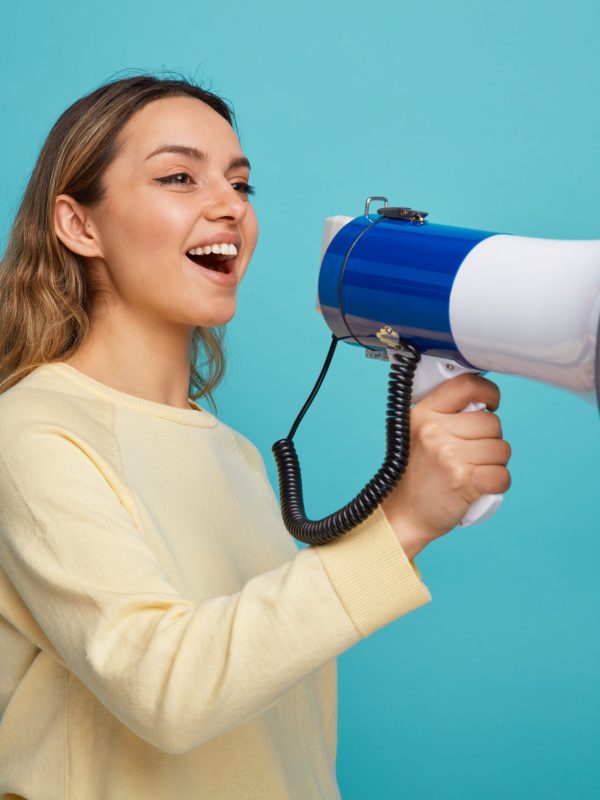 joyful young girl standing in profile view looking at side talking by speaker isolated on blue background joyful young girl standing in profile view looking at side talking by speaker isolated on blue background